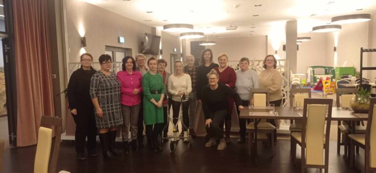 Zdjęcie grupowe 13 osób w restauracji. 12 kobiet i 1 mężczyzna. Przed jedną z kobiet balkonik.